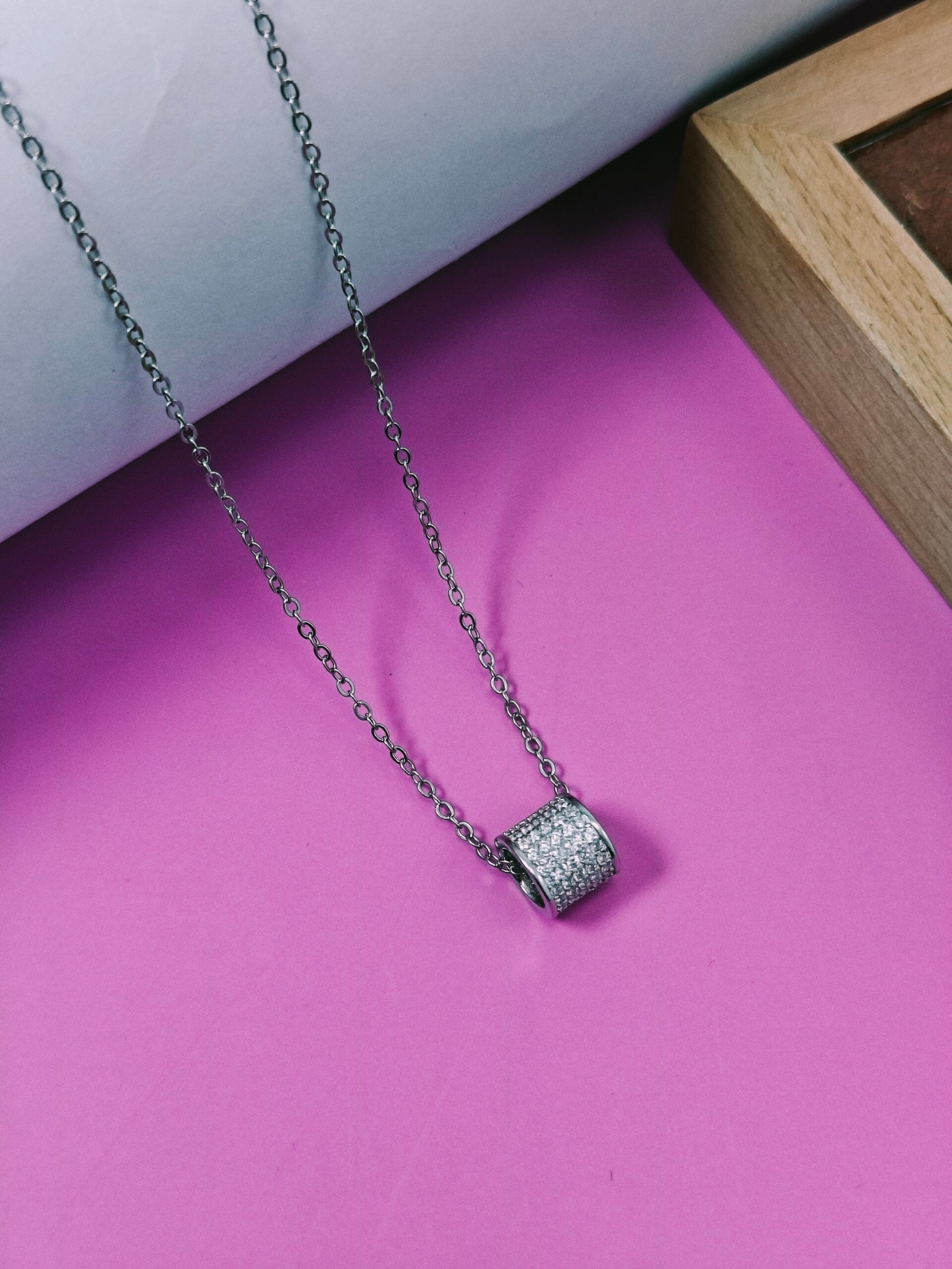 Silver necklace with a heart-shaped pendant on a pink surface